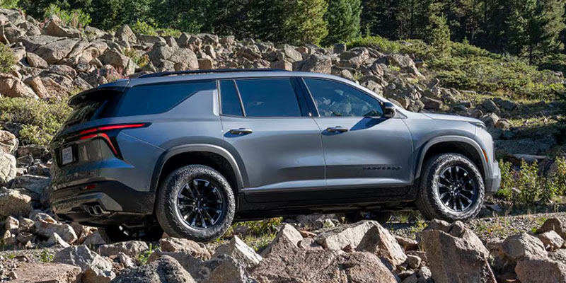 A grey Chevrolet Traverse Z71 parked on a rugged, rocky incline with a dense forest in the background.
